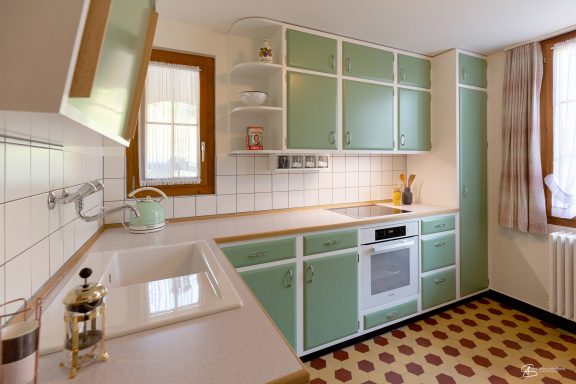 Moderne Küche mit grünen Schränken, weißer Arbeitsfläche und retro-fliesenboden.